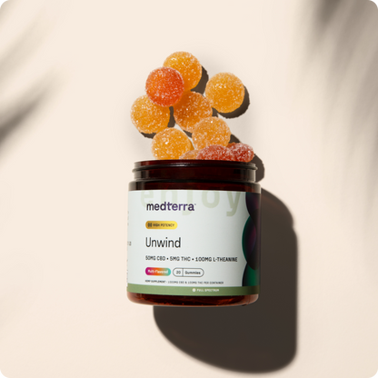 A jar labeled "Unwind CBD Gummies" by Medterra contains orange and red gummy supplements for stress relief, with ingredients listed as 50mg CBD, 5mg THC, and 100mg L-Theanine. Several sugar-coated gummies are scattered around the open jar, casting a shadow in the background.